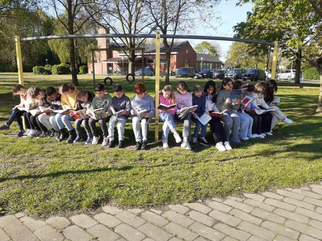 Leerlingen lezen buiten op een bank in het groen